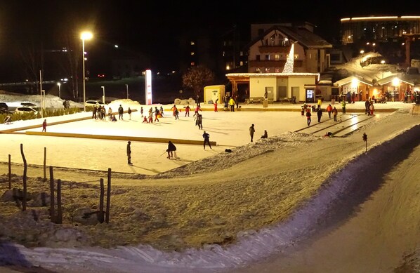 A snow-covered area with people, a building with a sloped roof, and a fence.