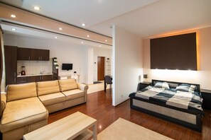 A modern living room with a sofa, a bed, and a small table. There is a kitchen area in the background.