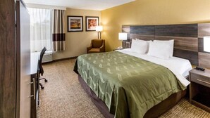Una habitación de hotel con cama, escritorio, silla, lámpara y mesita de noche.