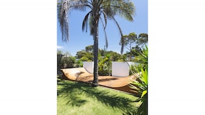 Un patio con una palmera, una terraza de madera curva y una pared blanca.