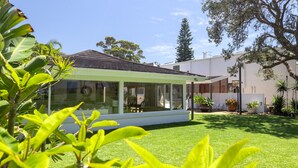 A modern house with a glass conservatory, a well-maintained lawn, and various potted plants.