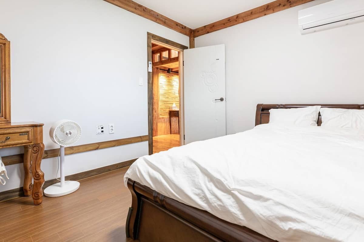 Ein Schlafzimmer mit einem hölzernen Bett, einem Nachttisch mit Ventilator, einem Spiegel und einer Klimaanlage.
