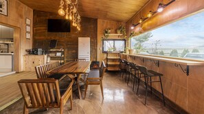 A wooden interior with a long dining table, chairs, a TV, and a view through a window. - Seogwipo Unyeong Pension (Seogwipo)