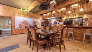 A wooden interior with a round dining table, chairs, a chandelier, a bar area, and a poster on the wall. - Seogwipo Unyeong Pension (Seogwipo)