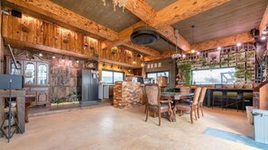 A rustic interior with wooden beams, a central dining table with chairs, and a kitchen area with a refrigerator and counter. - Seogwipo Unyeong Pension (Seogwipo)