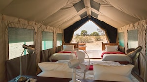 A tented accommodation with two beds, each with a pillow and a blanket, and a table with a lamp.