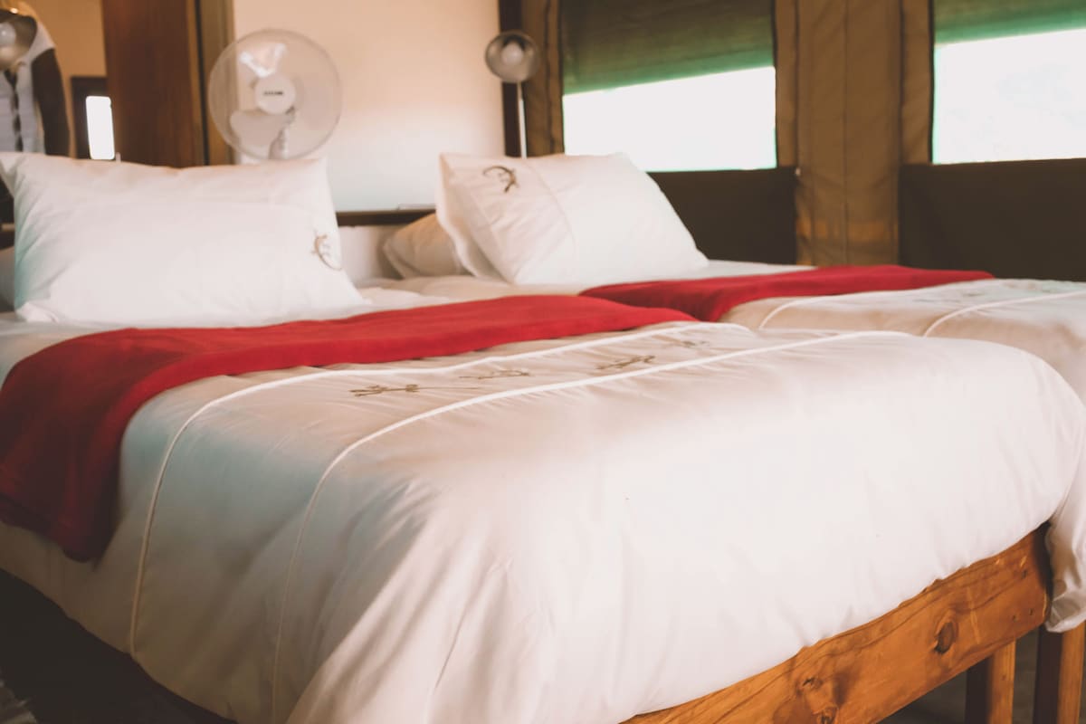 A bed with white bedding and a red blanket, a wooden headboard, and a wall-mounted fan.