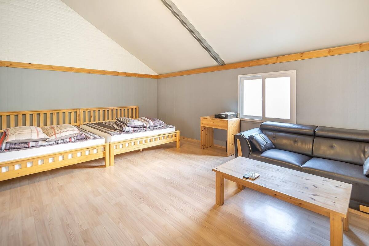 A small, well-lit room with a wooden bed, a leather sofa, and a wooden table.