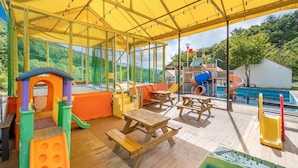 An outdoor patio area with picnic tables, a children's play structure, and a pool. - Pocheon Kidsglampinggeo (Pocheon)