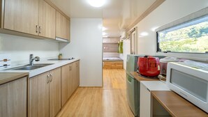 A compact kitchen with wooden cabinets, a sink, and a window with a view of greenery. - Pocheon Kidsglampinggeo (Pocheon)