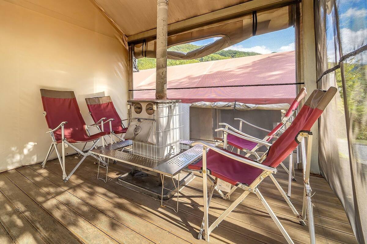A covered outdoor seating area with metal chairs and a table, a metal grill, and a view of the outdoors.