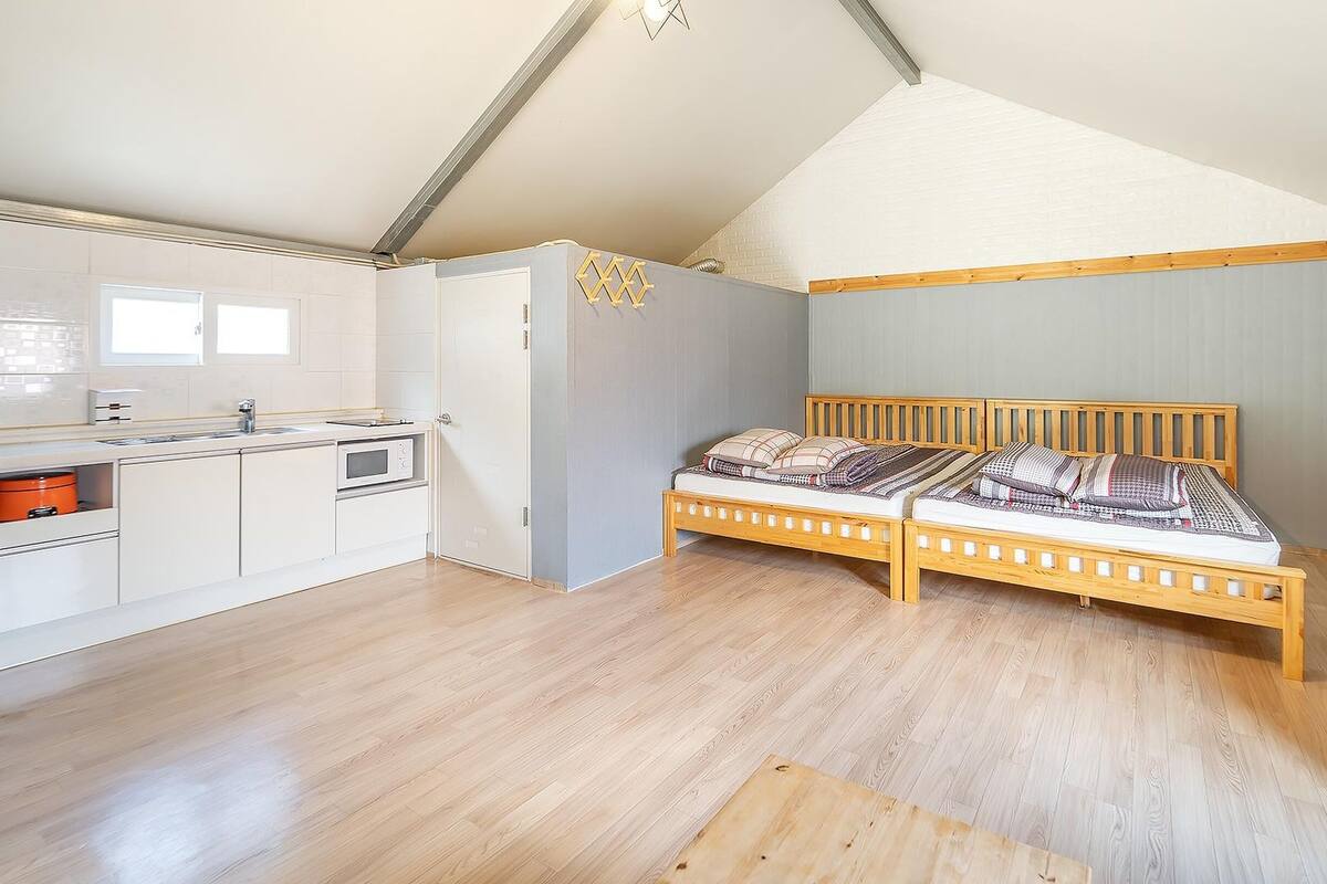 A compact room with a kitchenette, a bed with a wooden headboard, and a sloped ceiling.