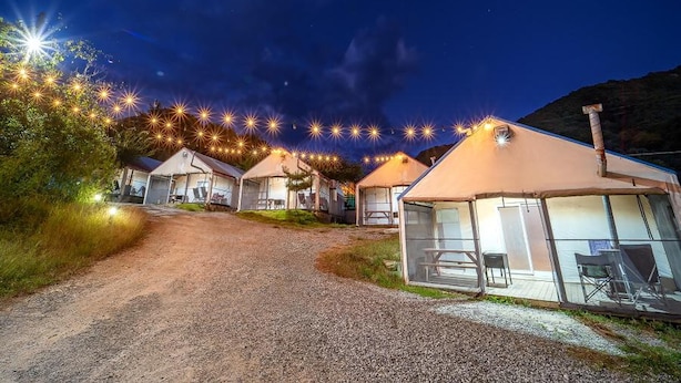 A row of cabins with a gravel path leading to them, surrounded by greenery and a mountainous backdrop. - Pocheon Kidsglampinggeo (Pocheon)