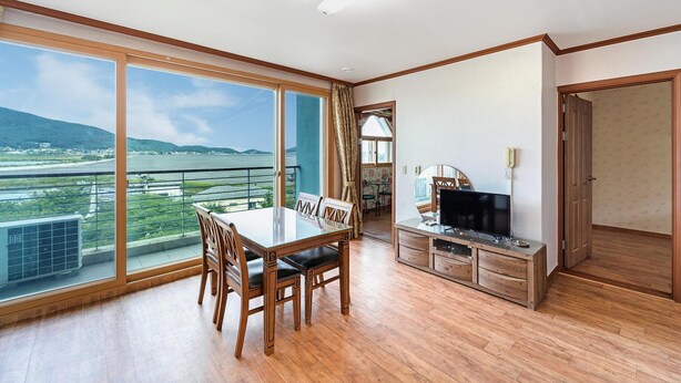 A spacious room with a balcony offering a view of a body of water and distant hills. - Ganghwa Dondaemoru Pension (Incheon)