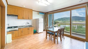 A kitchen with wooden cabinets, a stove, and a refrigerator. There's a dining table with chairs and a large window offering a view of a landscape. - Ganghwa Dondaemoru Pension (Incheon)