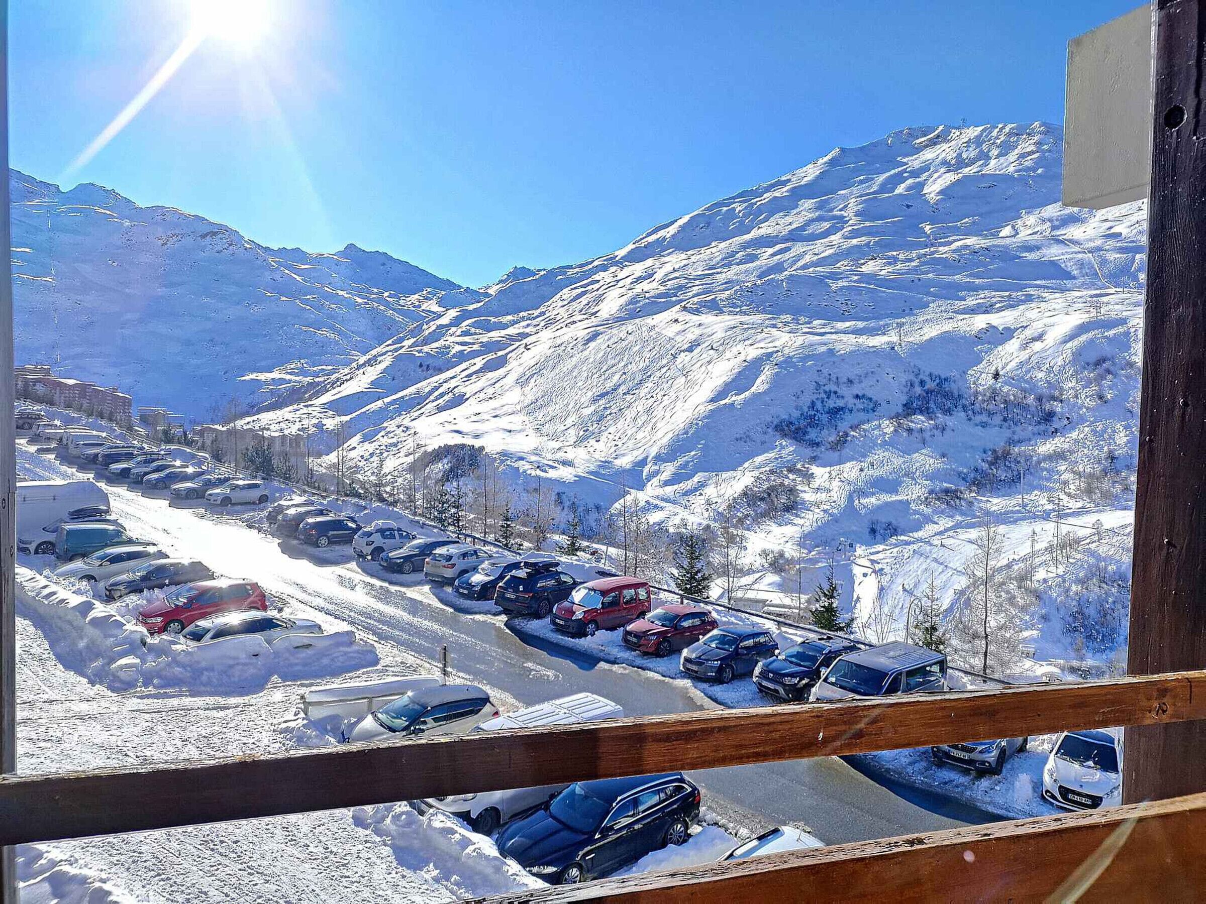 A view of a snow-covered parking lot with cars and mountains in the background.