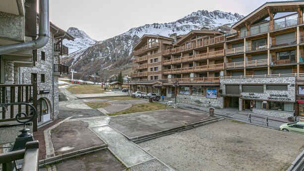A mountain resort with multi-story buildings, a paved square, and snow-capped mountains in the background.