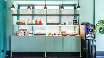Een keuken in blauwgroen met een glazen vitrine, een koffieapparaat en een plant.
