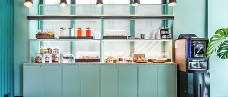 Une cuisine aux tons bleu-vert, avec un meuble vitré, une machine à café et une plante.