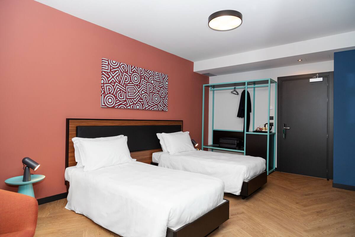 A hotel room with two beds, a wardrobe, a desk, and a wall art piece.