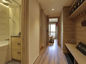 Un pasillo con piso de madera, un banco y un cartel, y vista a una habitación con cama.
