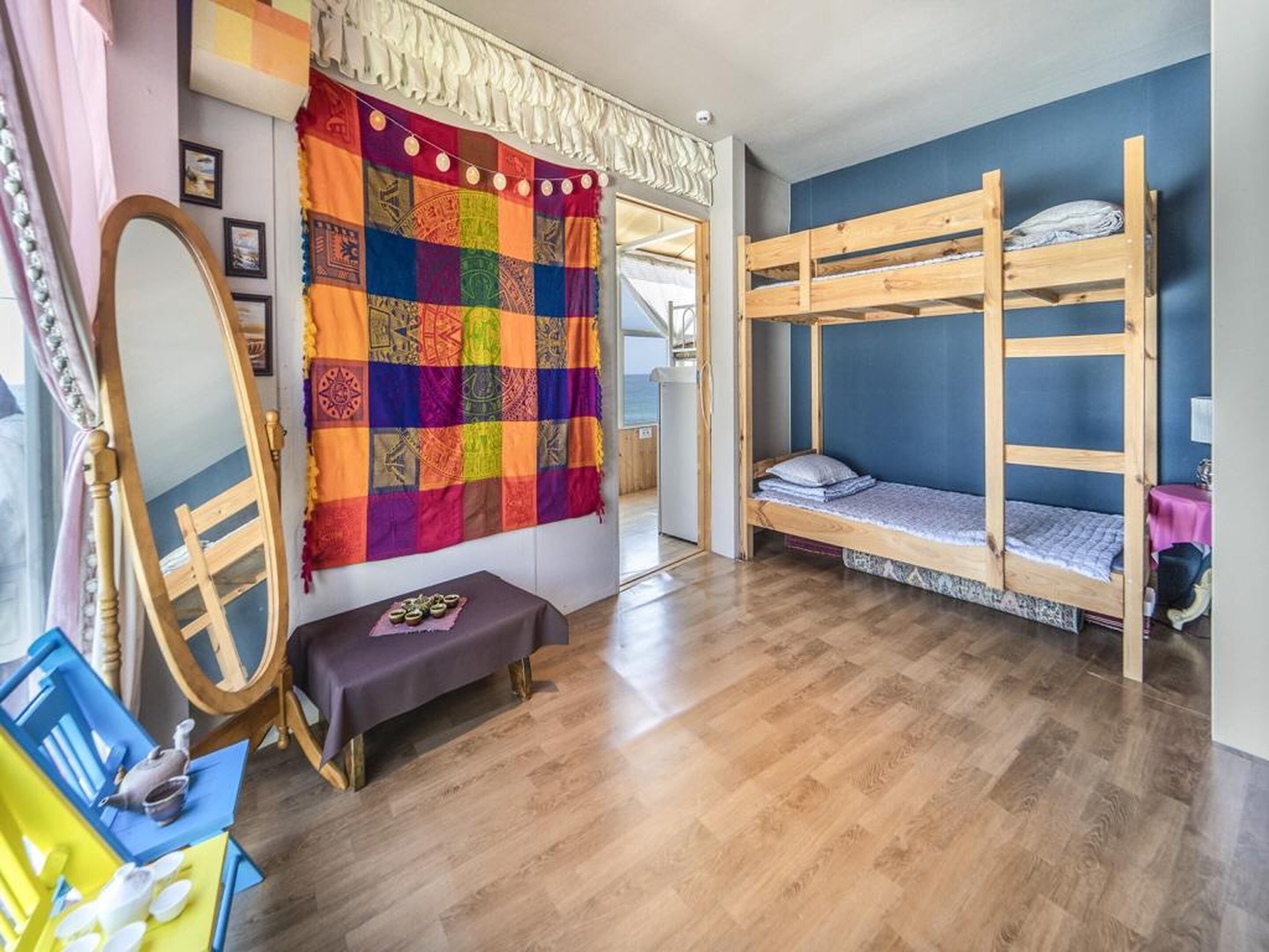 A room with a bunk bed, a colorful quilt, a mirror, and a small bench.