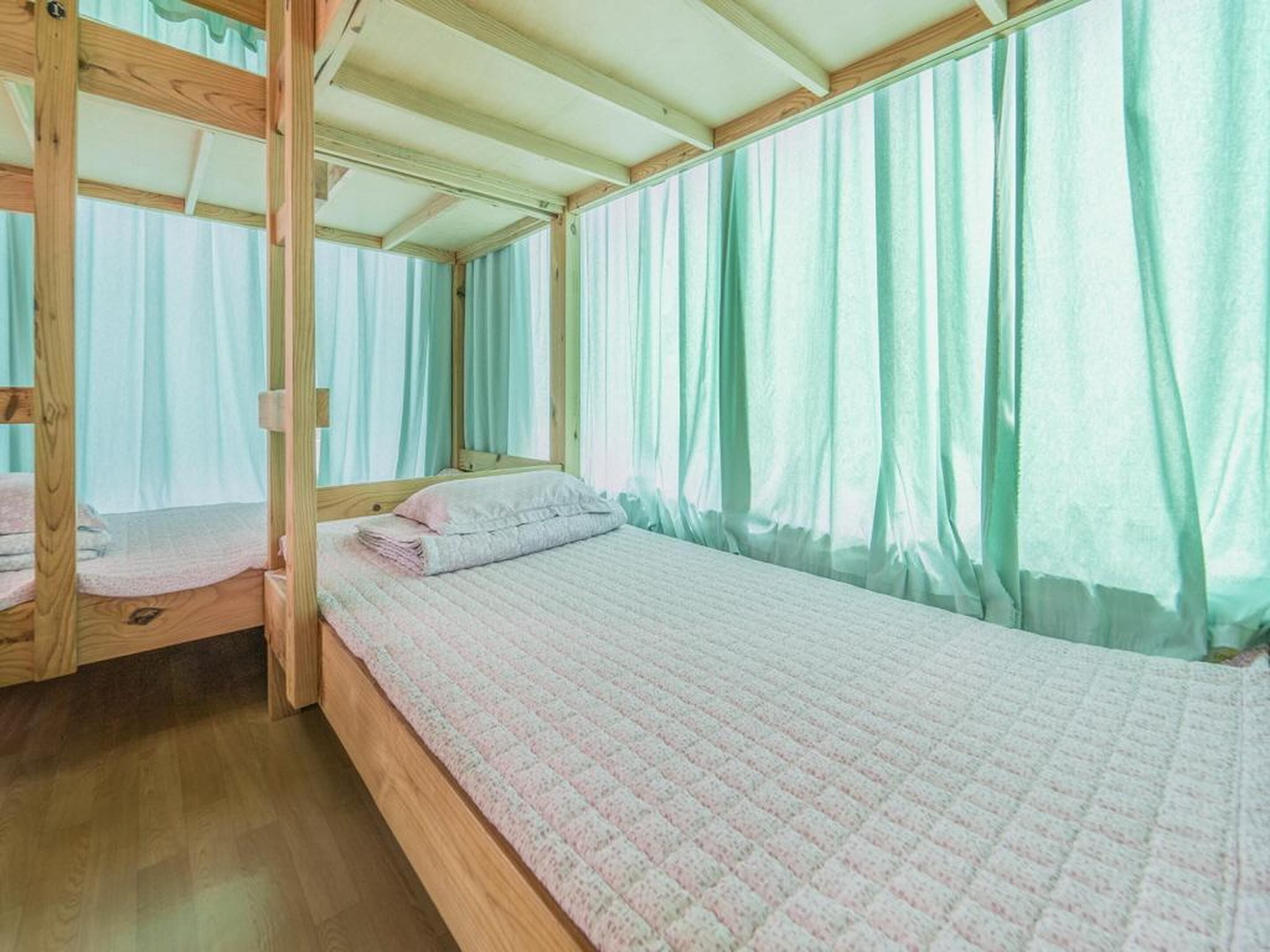 Ein Einzelbett mit Decke, einem Holz-Kopfteil und einem Fenster mit durchsichtigen Vorhängen.