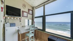 Una habitación pequeña con piso de madera, una mesita, una silla, un sofá, un televisor y ventana con vista a la playa.