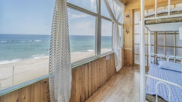 Una cabaña con interior de madera, una litera y un amplio ventanal con vistas a la playa.