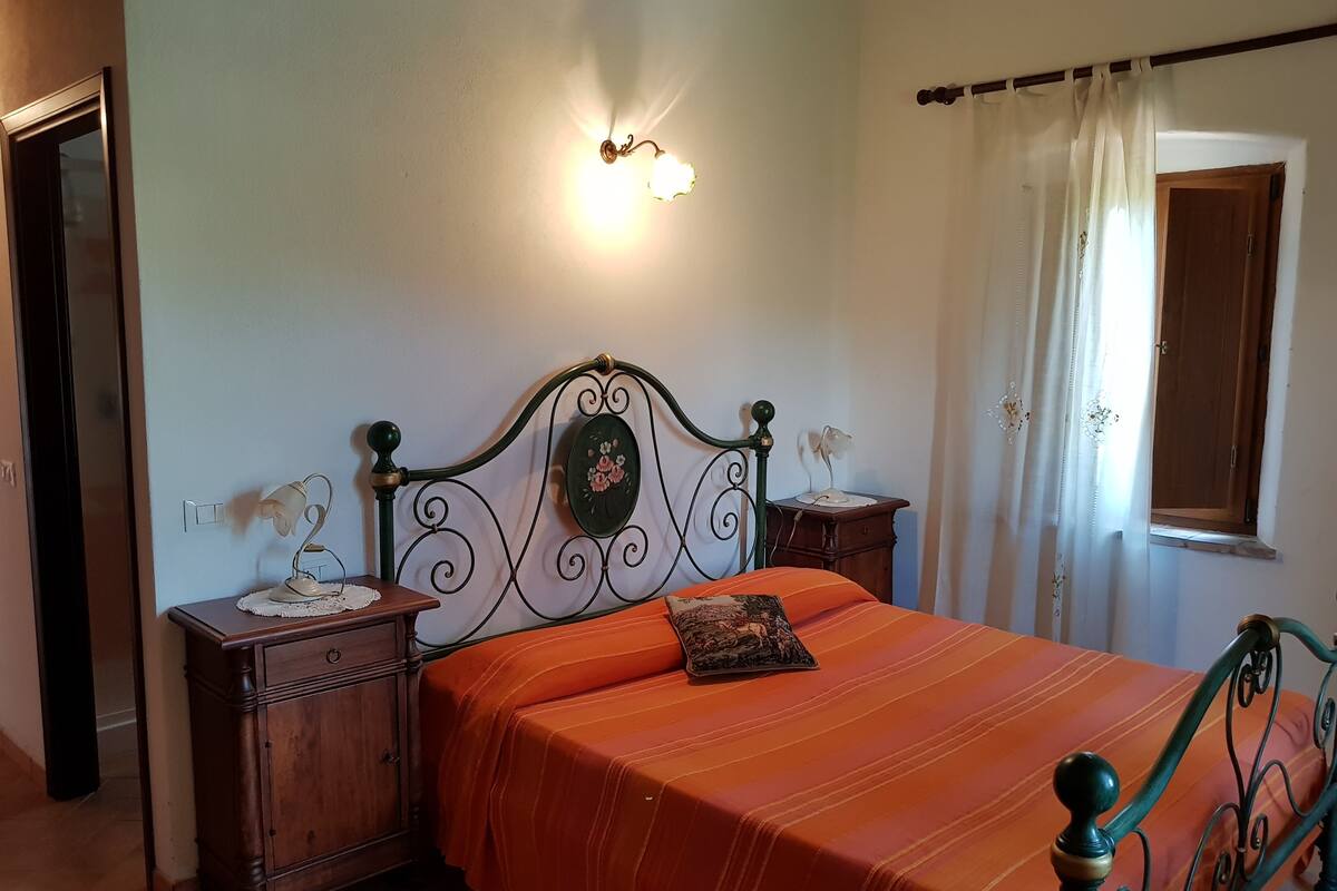 Une chambre à coucher comprenant un lit, des tables de chevet, une lampe fixée au mur, une fenêtre avec des rideaux et une porte.