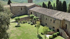 A historic stone building with a courtyard, surrounded by trees and set against a rural landscape.