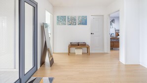 A hallway with wooden flooring, a bench with baskets, and three wall-mounted paintings. - Jeju Jongdalrifeel House (Jeju City)