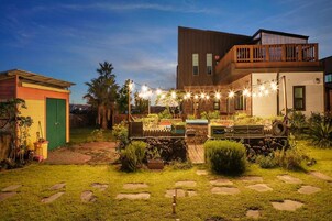 A modern house with a backyard featuring a stone pathway, a small garden, and string lights.