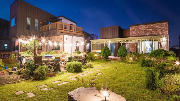 A modern residential complex with multiple buildings, a well-maintained garden with stepping stones, and outdoor lighting. - Jeju Jongdalrifeel House (Jeju City)