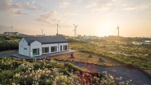 A modern house with a large deck, surrounded by wind turbines and natural landscape.