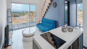 A modern kitchen with a built-in stove, a blue sofa, and a staircase leading to another level.