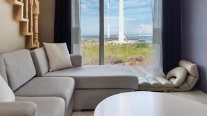 A modern living room with a sectional sofa, a round coffee table, and a view of a coastal landscape through large windows.