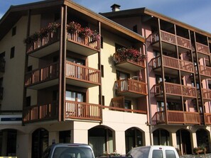 Ein mehrstöckiges Hotel mit Balkonen, Rundbogenfenstern und einem Parkplatz.