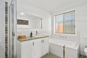 Features a large mirror, sink, bathtub, and toilet in a sleek, white design.
