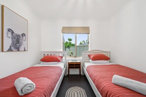 Two single beds with white headboards and red bedding, a nightstand, and a window with a blind.