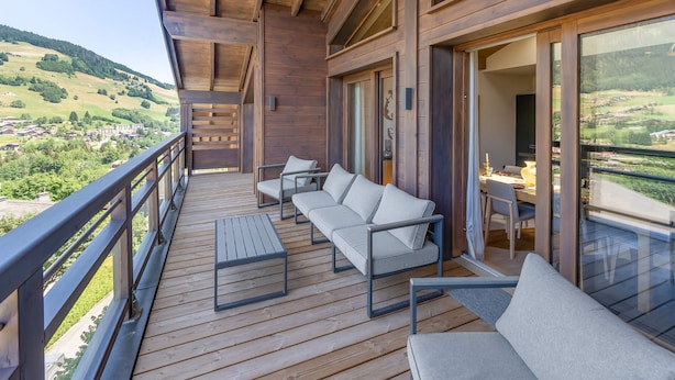 A wooden deck with a sofa and table, overlooking a scenic valley. - Duplex in Megève with spa, pool, gym and fireplace (Megève)