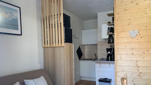 A compact living space with a sofa, a small kitchen area, and a wooden wall. - Renovated mezzanine studio for 4, near gondola in Pra Loup (Pra-Loup)