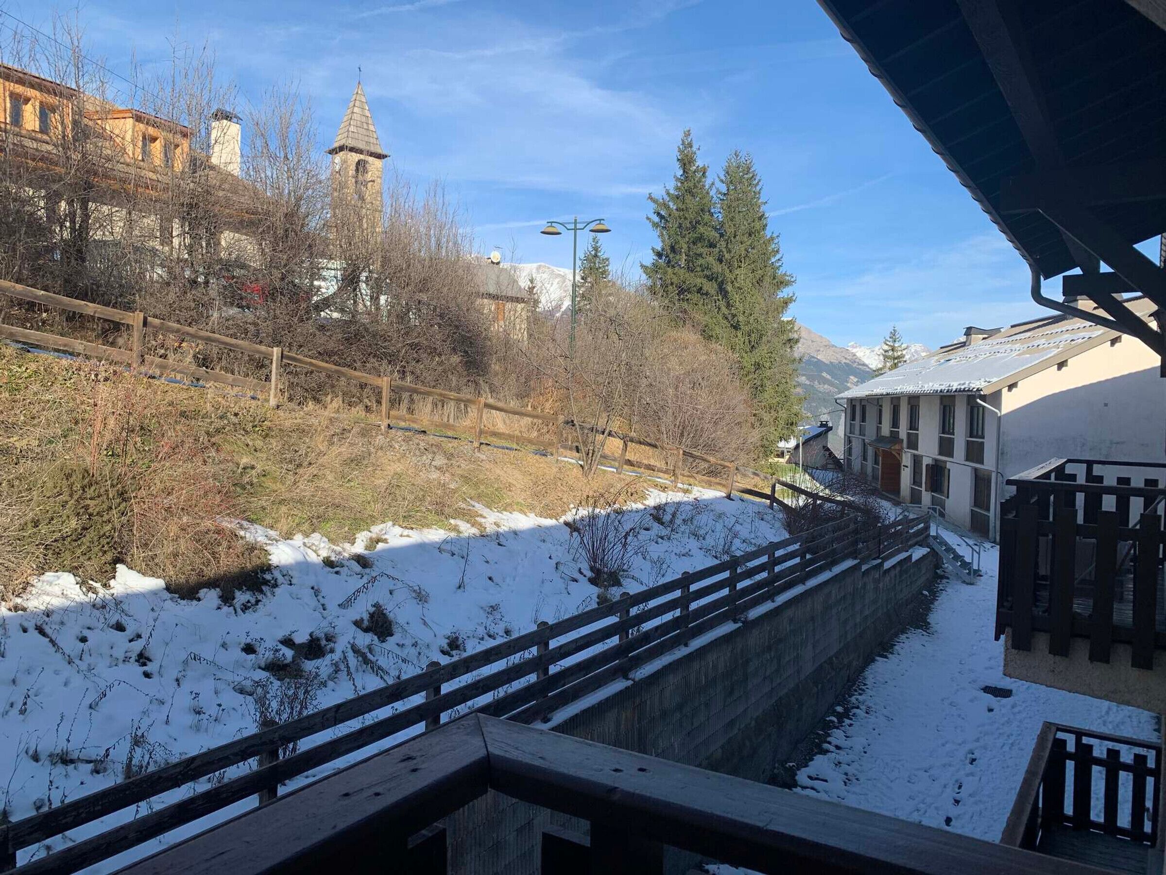Un paysage enneigé avec une clôture en bois, le clocher d’une église et un bâtiment doté d’un toit en pente.