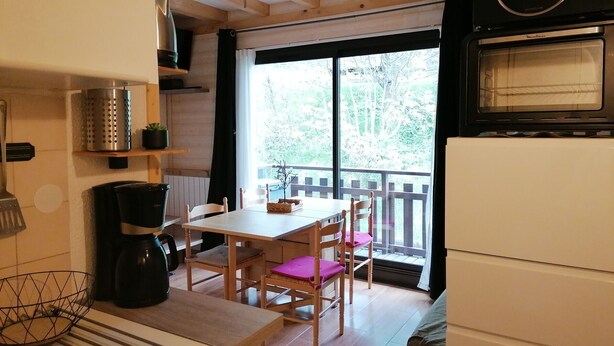 A compact kitchen with wooden cabinets, a dining table with chairs, a large window with a view of trees, and a microwave. - Renovated mezzanine studio for 4, near gondola in Pra Loup (Pra-Loup)