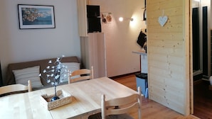 A cozy living area with a wooden table, chairs, a sofa, and a wall-mounted TV. - Renovated mezzanine studio for 4, near gondola in Pra Loup (Pra-Loup)