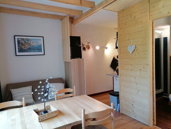 A cozy living area with a wooden table, chairs, a sofa, and a wall-mounted TV.