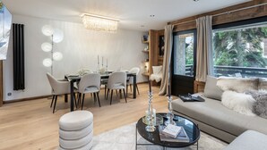 A modern living room with a dining area, a chandelier, and a large window with curtains. - Charming 3-BR Apartment in Megève, Near Center, Ski, and Sports Complex (Megève)