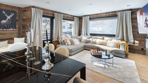 A modern living room with a large sectional sofa, a dining table with candles, and a chandelier. - Charming 3-BR Apartment in Megève, Near Center, Ski, and Sports Complex (Megève)