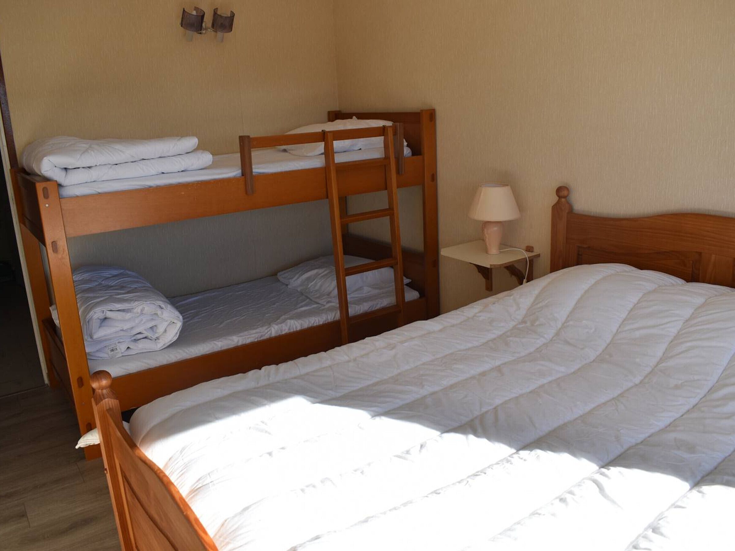 A bunk bed room with a single bed, a nightstand with a lamp, and a wall-mounted shelf.