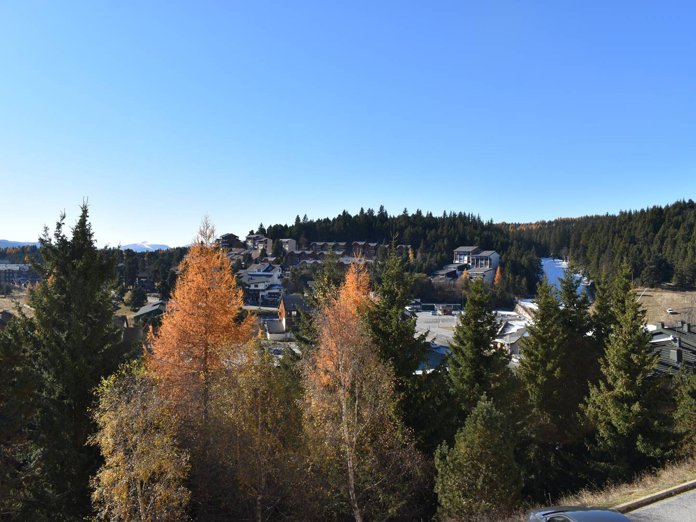Ett bostadsområde med hus, en parkeringsplats och en skogbeklädd kulle i bakgrunden.